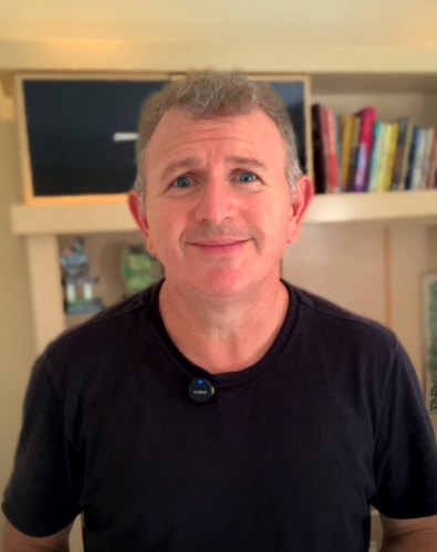 Marcio Geteski, fundador da Academia do Massoterapeuta, sorrindo diante de uma estante de livros